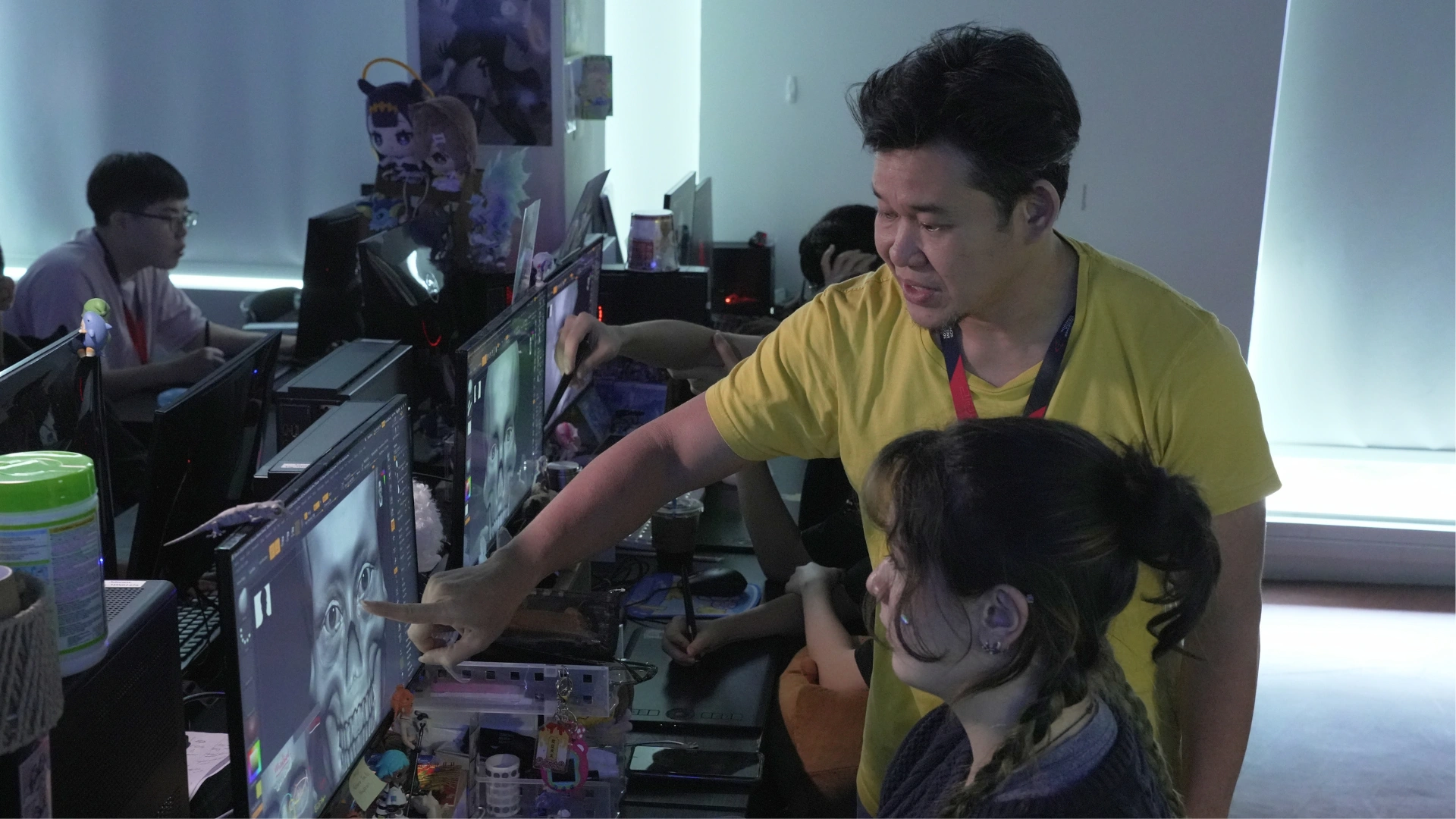 A 3dsense lecturer guiding a student by pointing at the monitor as others work intently at their computer stations.