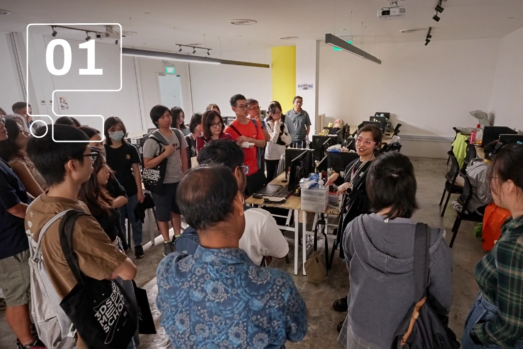A group of people attentively listens to a speaker in a spacious room with computers, fostering an engaging environment.