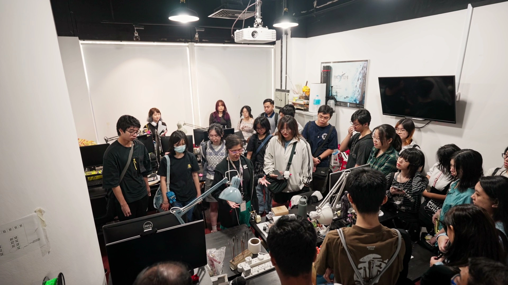 A crowded room filled with people gathered around a table with various equipment, tech gadgets, and monitors.