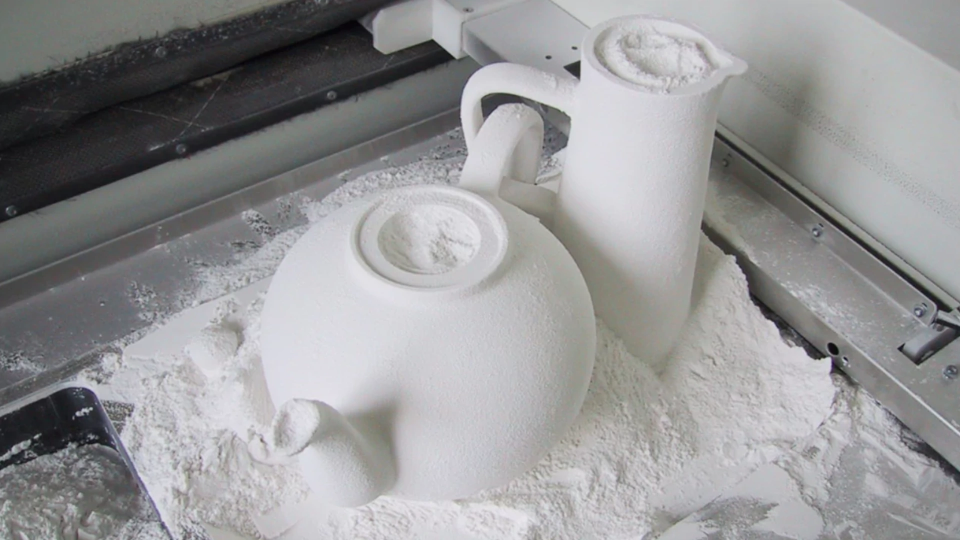 An abstract white teapot and pitcher, partially embedded in fine white powder, on a work surface with scattered residue.