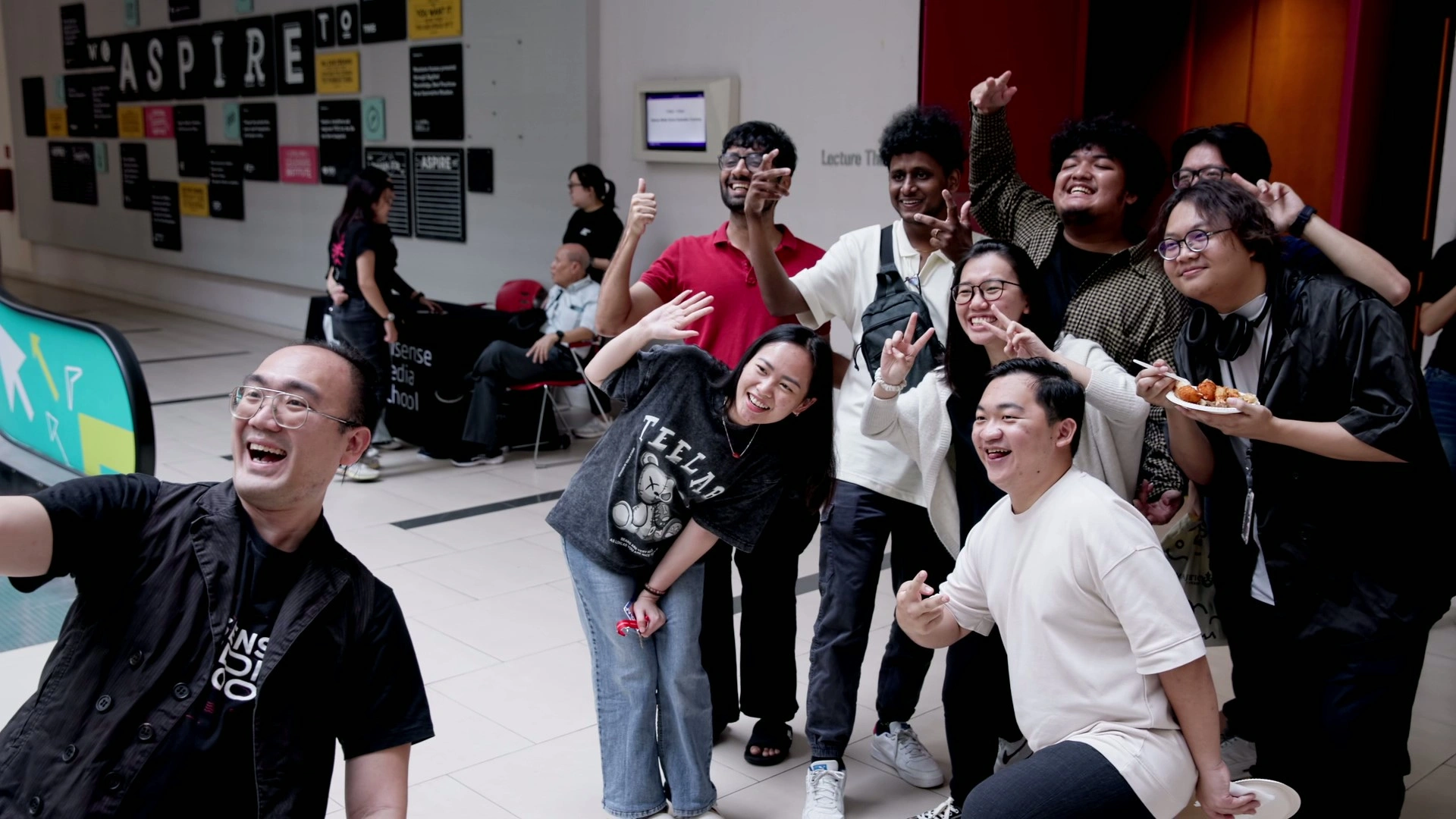 A group of students poses playfully for a photo in a lively indoor setting, showcasing various gestures and smiles.