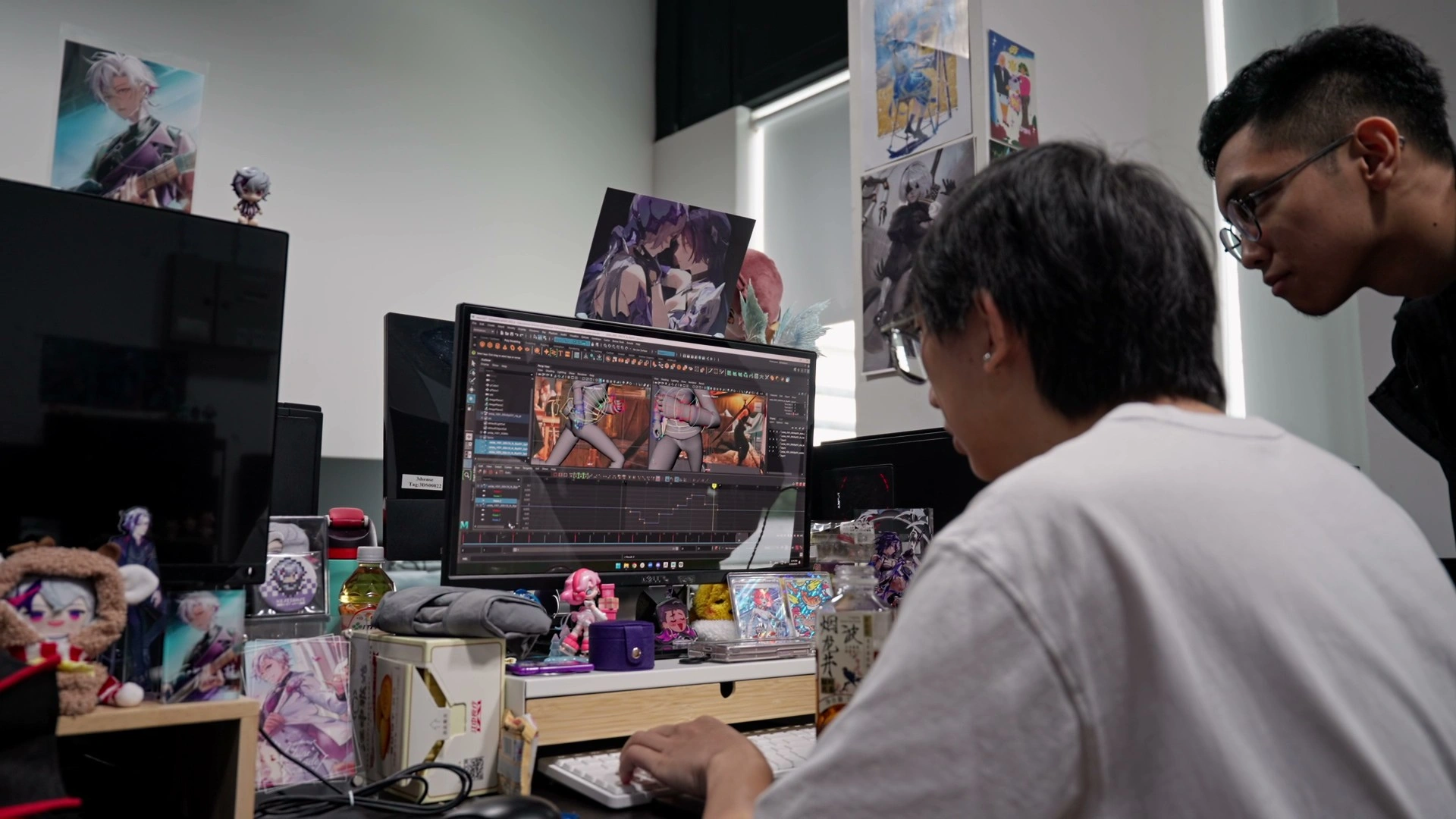 A student sits at a cluttered desk, editing a 3D animation on a computer, surrounded by figurines and colorful artwork.