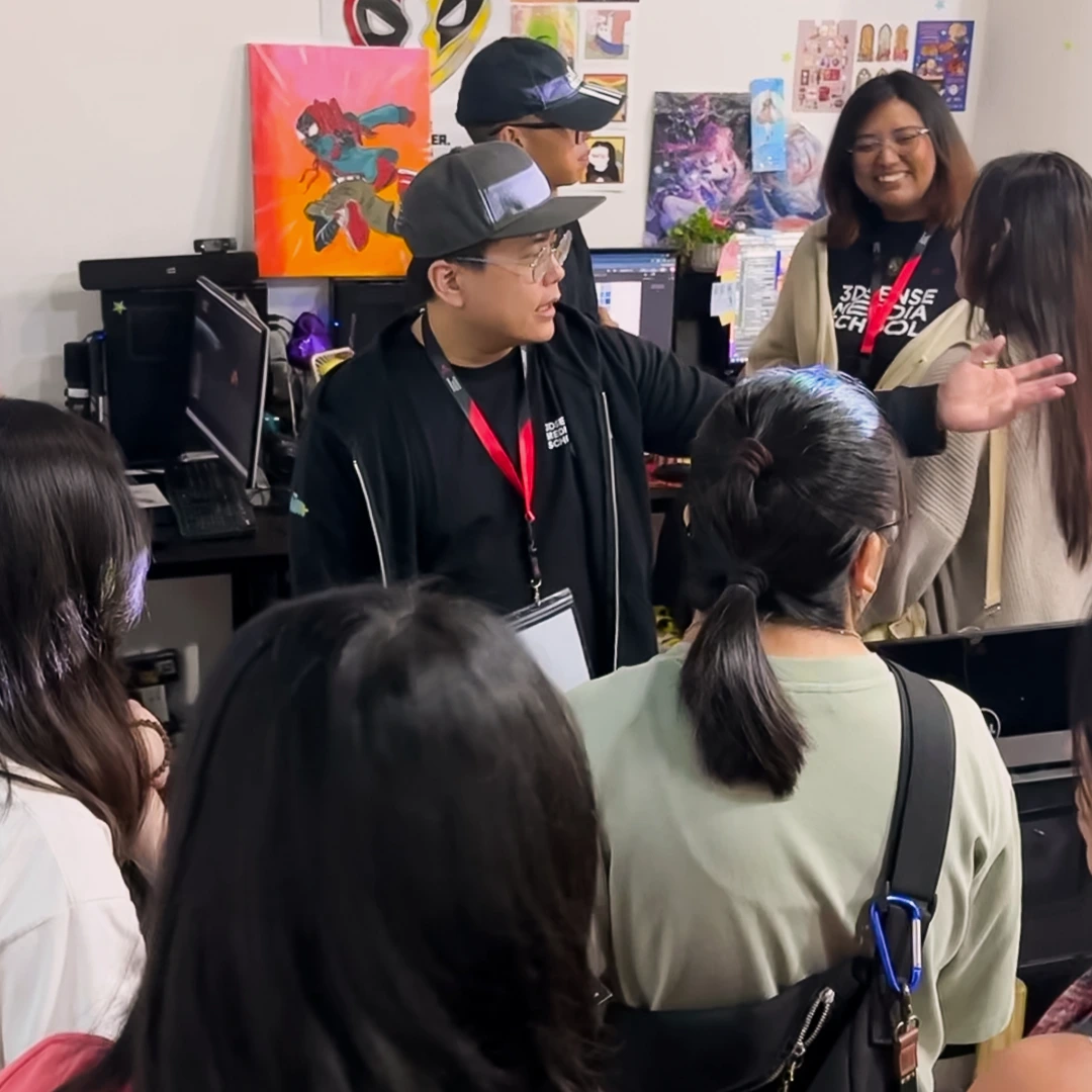 A group of people engage in conversation in a creative workspace decorated with colorful artwork and computers.