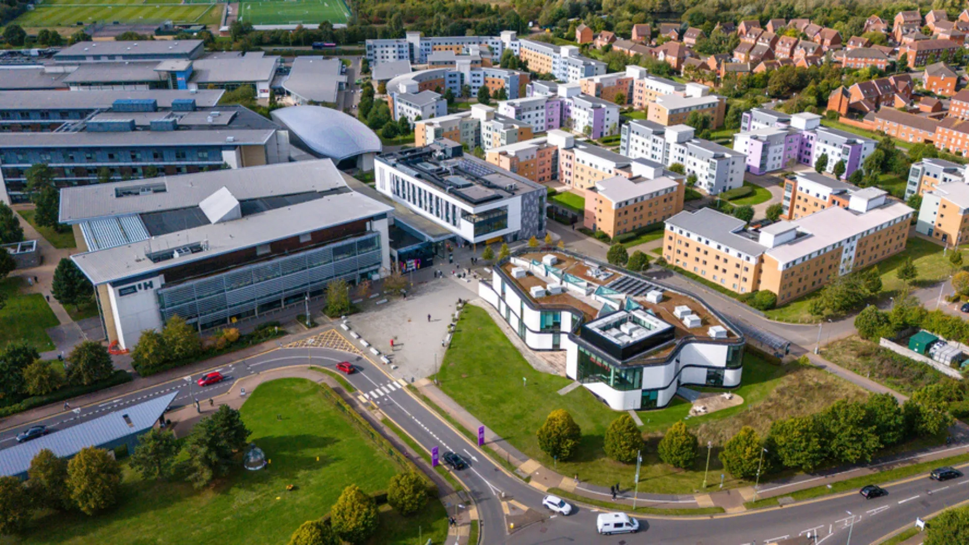 Aerial view of a university campus featuring modern buildings, green spaces, and nearby residential blocks.