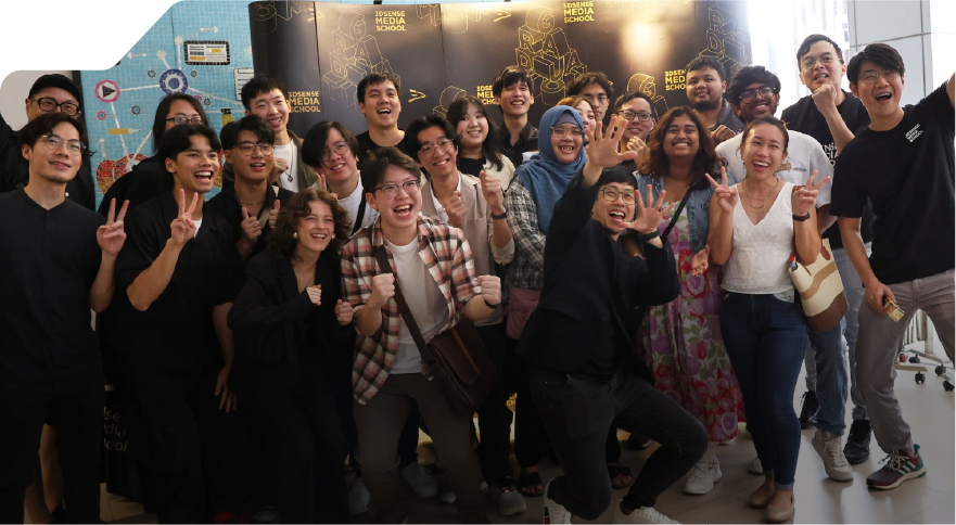 A group of people smiling and celebrating indoors, posing energetically with peace signs and thumbs up. The background features a modern, tech-themed wall. Bright and joyful atmosphere.