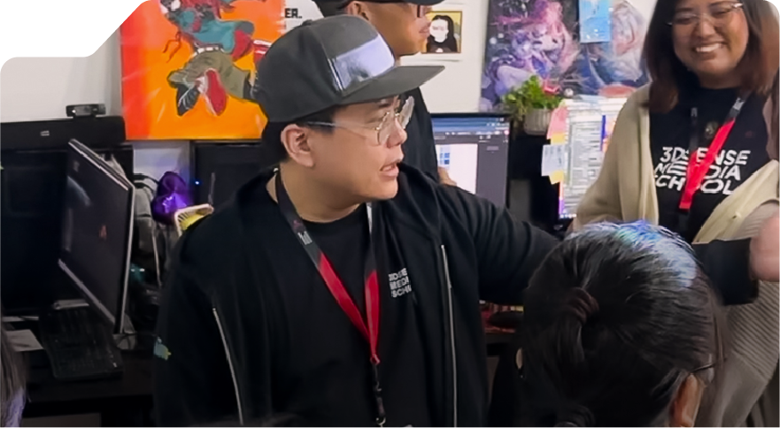 A group of people in a room with art-covered walls engage in animated conversation. Laptops and colorful posters create a lively, creative atmosphere.